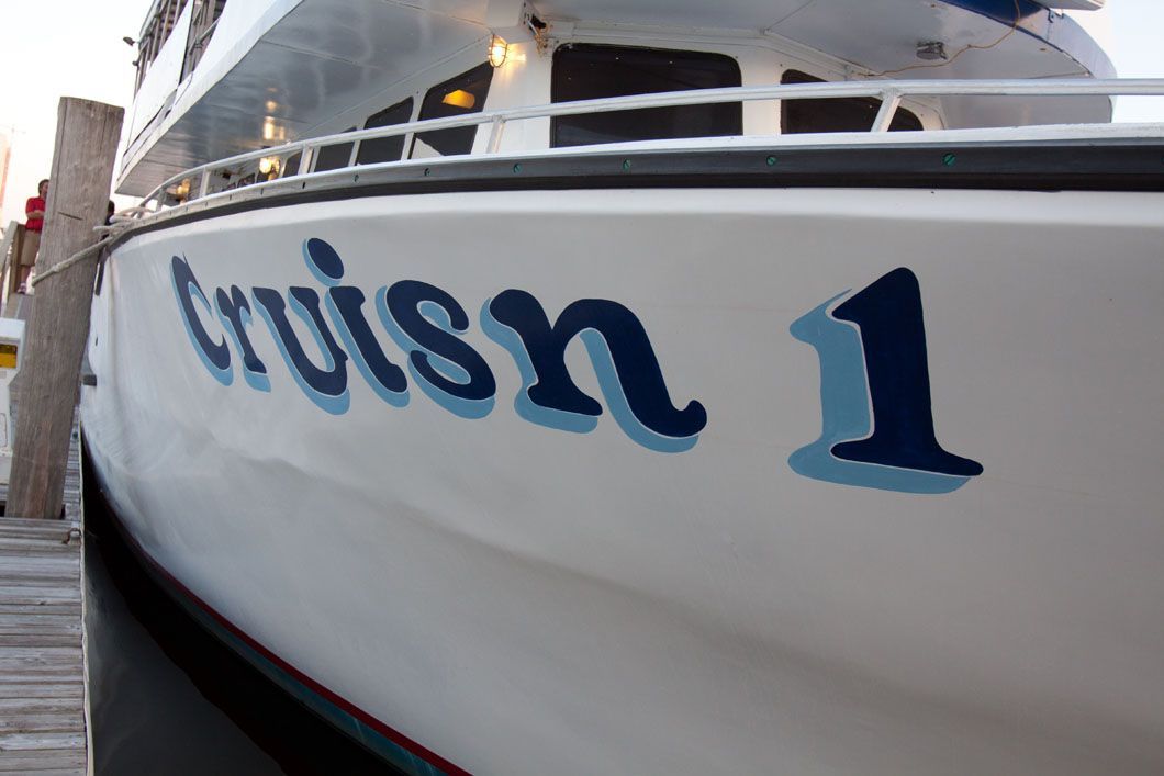 White boat with "Cruisn 1" in blue letters at a dock.