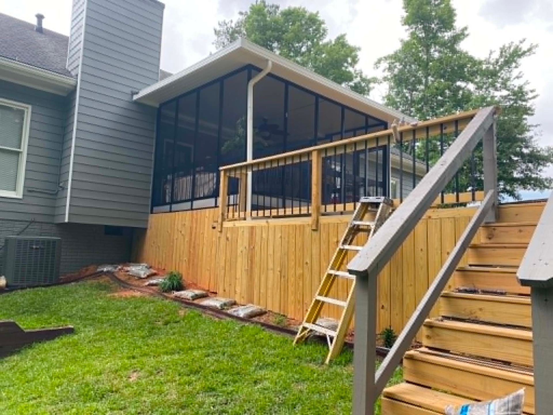 Backyard deck with screened porch, wooden railing, and exterior stairs beside a house