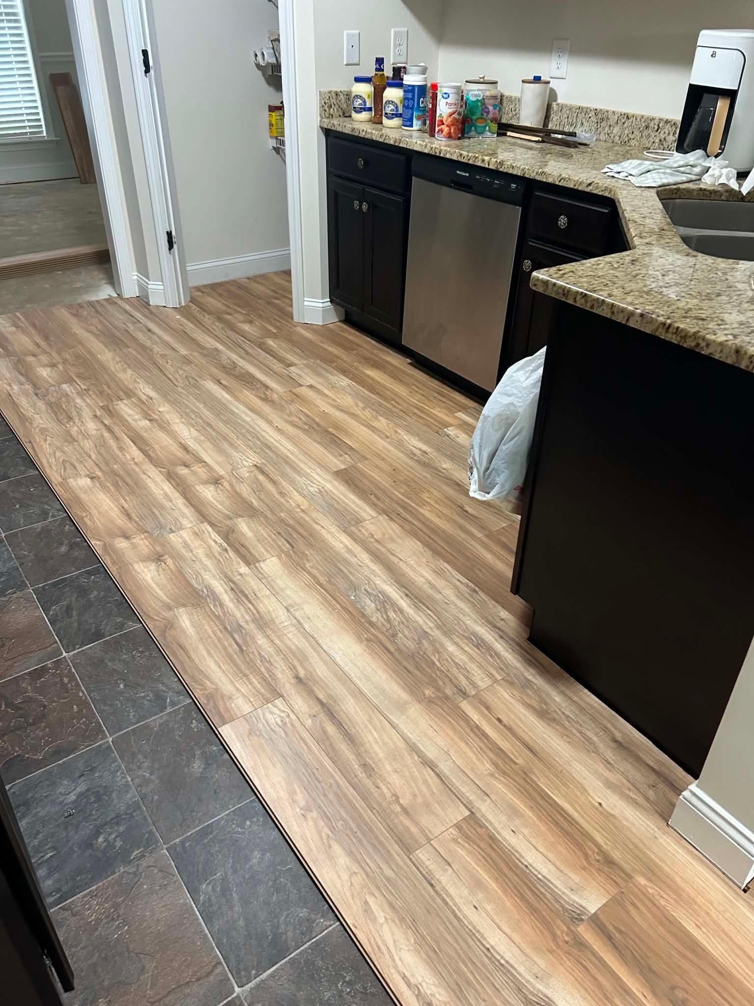 Kitchen with granite counters, black cabinets, wood-look flooring, and a trash bag hanging from a cabinet handle.