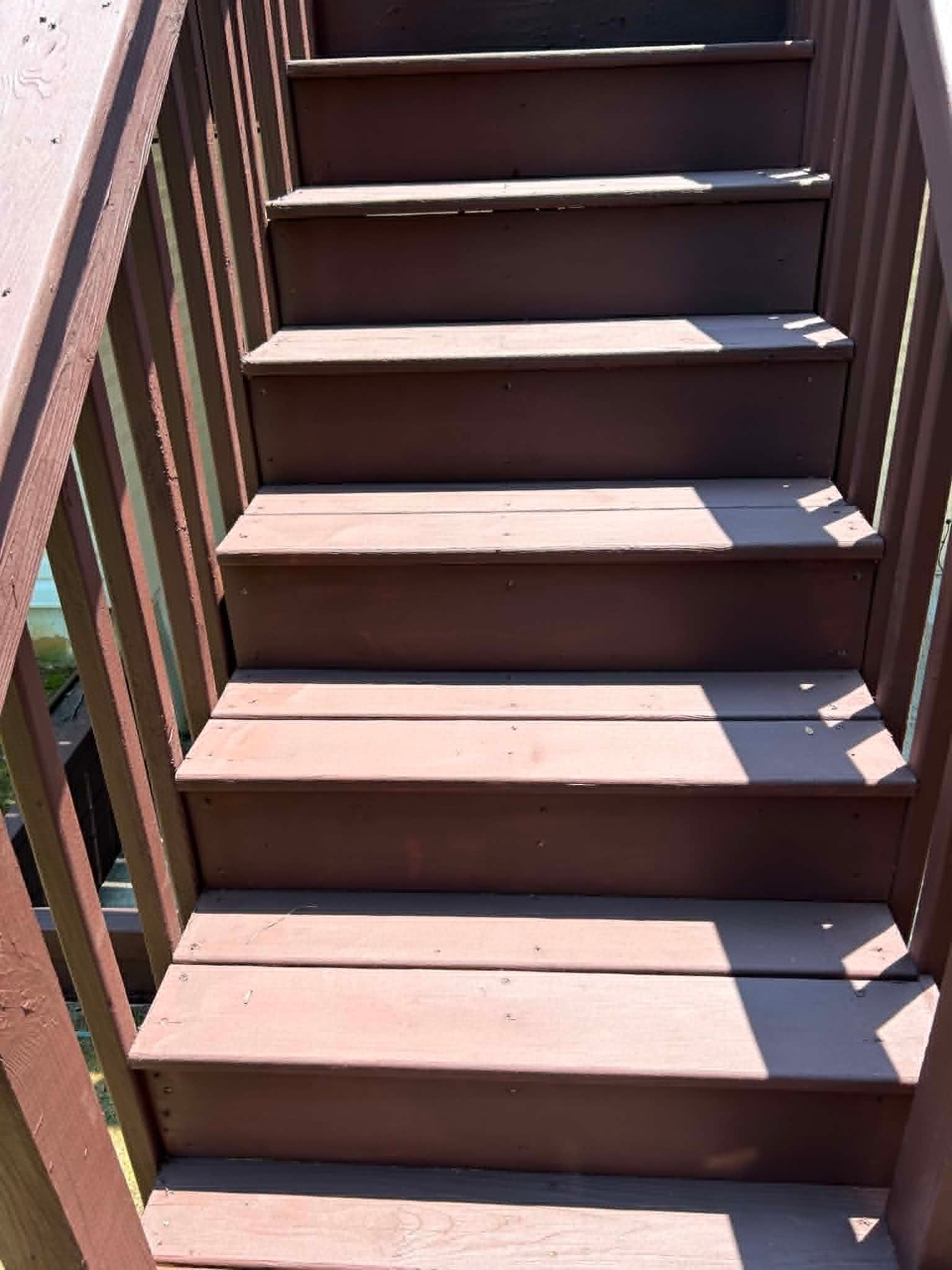 Wooden outdoor staircase with brown steps and railings in bright sunlight.