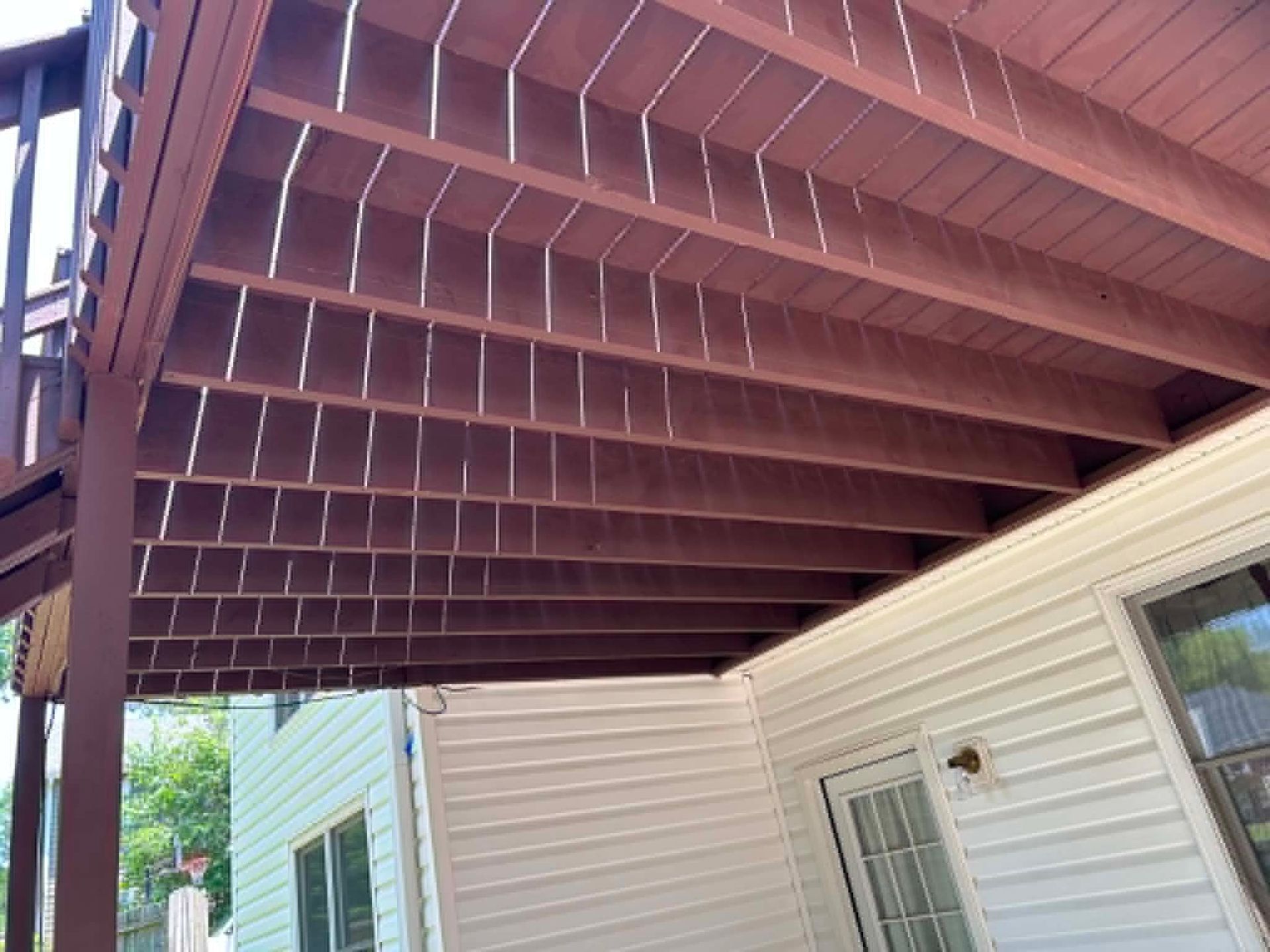 Wooden pergola over a white house patio with siding and windows