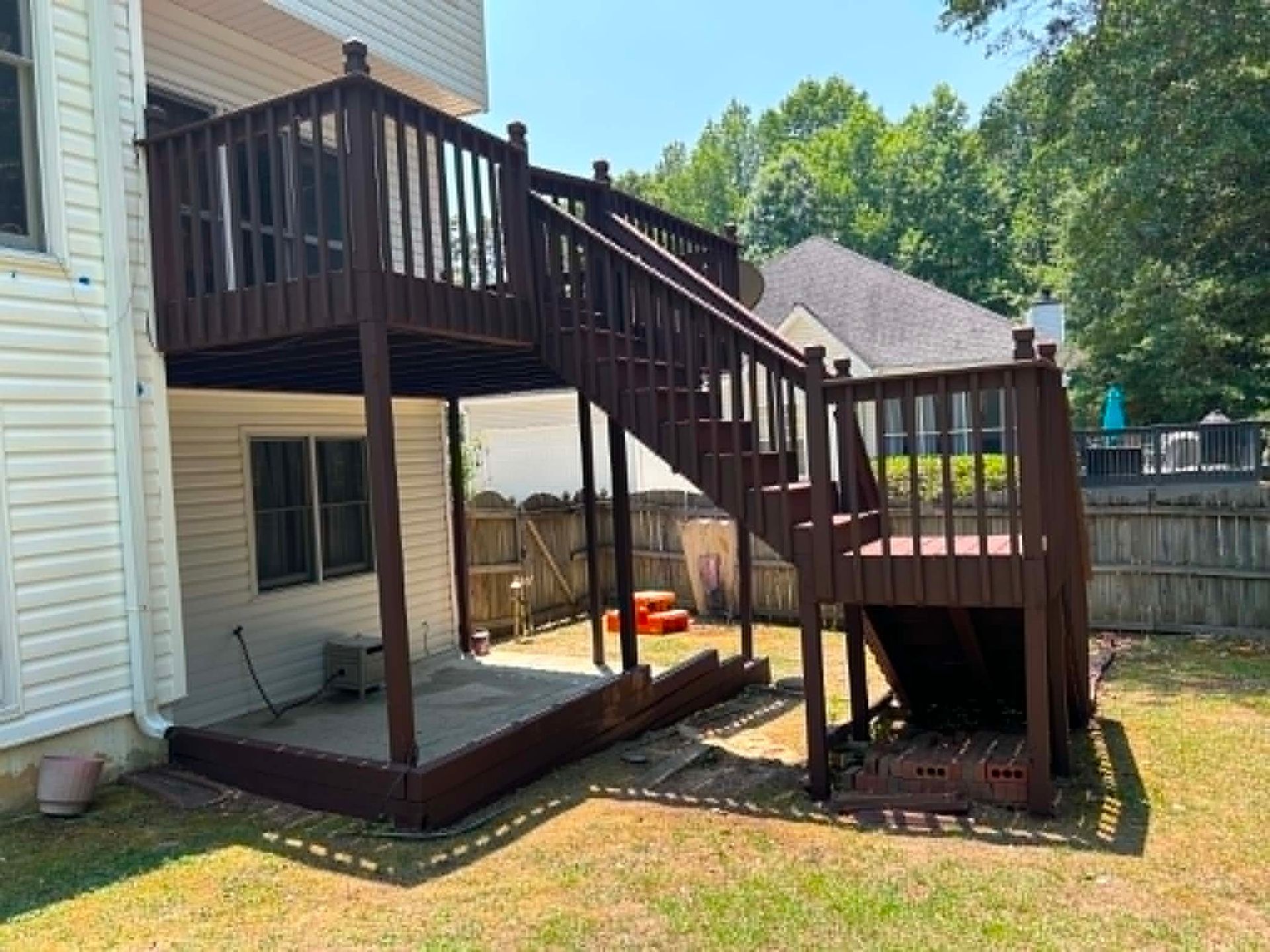 Backyard raised wooden deck with stairs, lower patio, and fenced yard beside a house