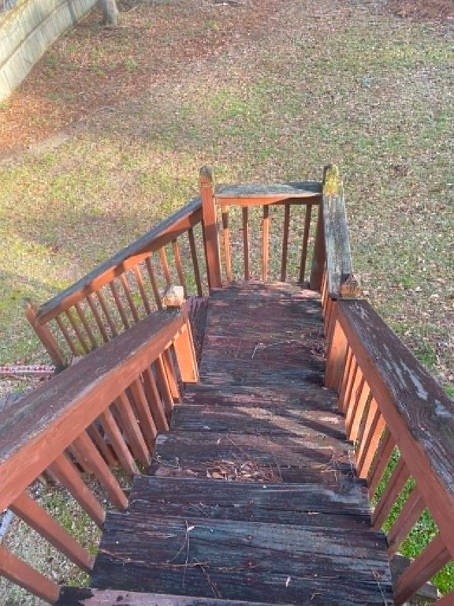 Wooden staircase descending to a grassy yard, with weathered dark steps and railings in sunlight