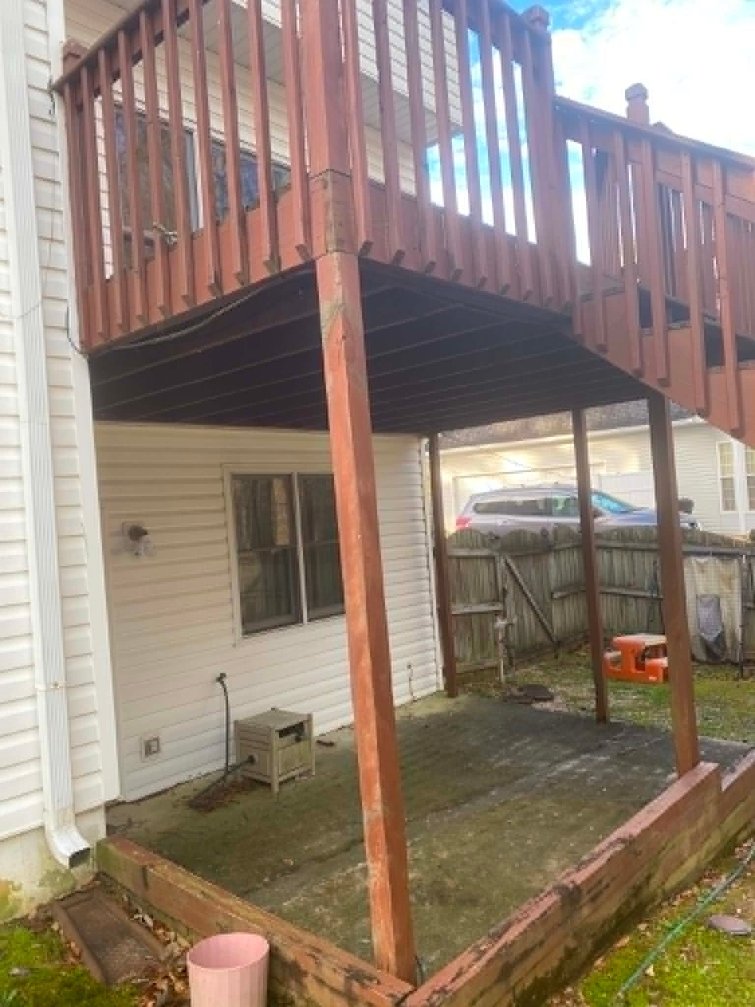 Wooden deck above a small fenced backyard patio beside a white house