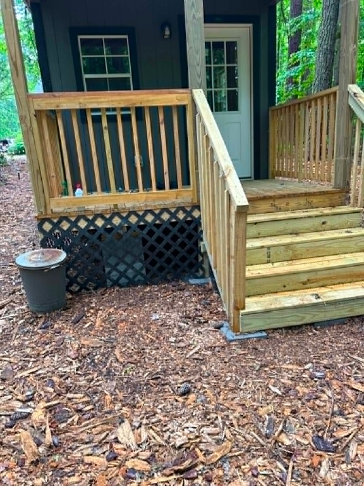 Wooden cabin porch with ramp, steps, railing, and black lattice skirting in a wooded setting