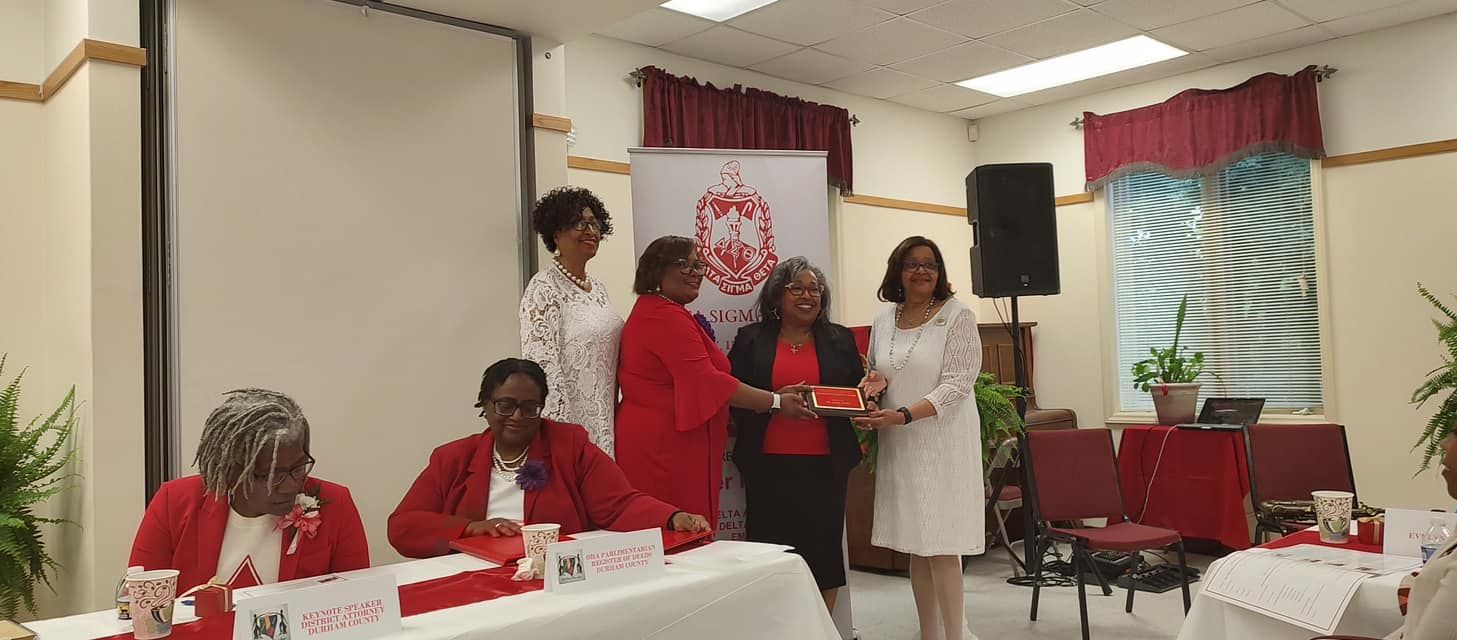 Group of women in red and white attire at an event. One woman receives a gift.