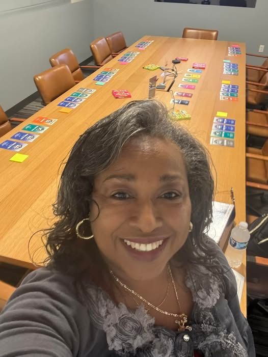 Smiling woman taking a selfie in a large conference room with colorful sticky notes on the table.