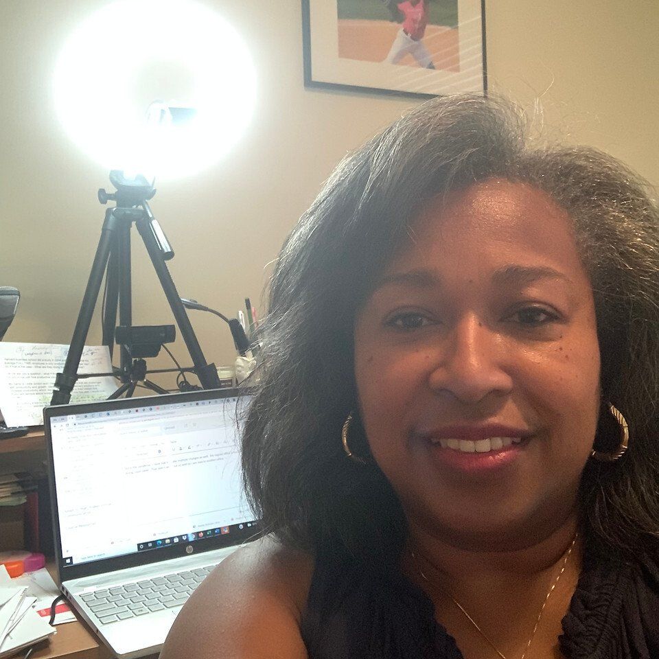 Woman with graying hair smiles in front of a laptop and ring light at a desk.