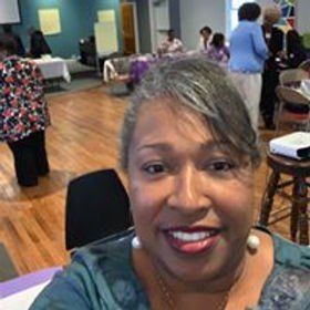 Smiling Black woman in teal shirt; group event in background.