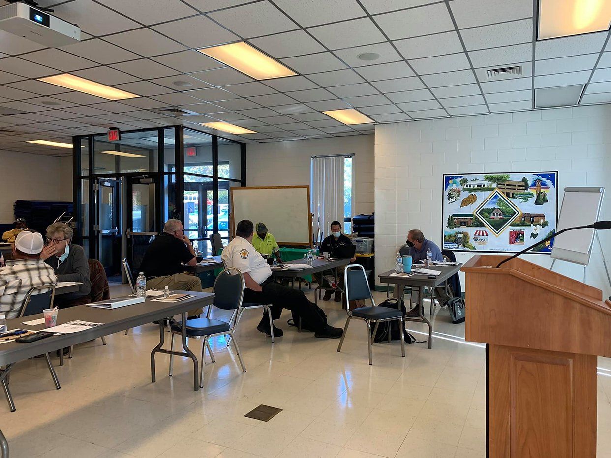 Meeting with people at tables in a brightly lit room. A presentation poster is visible.