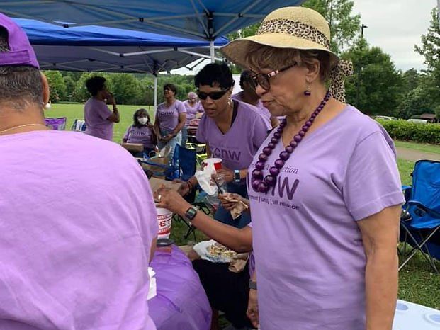 People in purple shirts at an outdoor event, some eating, under a tent.