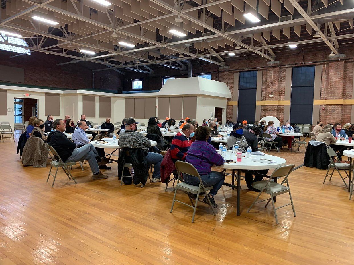 People seated at tables in a large hall, likely attending a meeting or event.