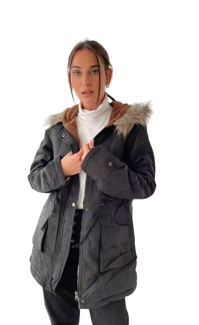 Mujer que lleva un abrigo negro con capucha ribeteada de piel, un jersey de cuello alto blanco y pantalones negros.