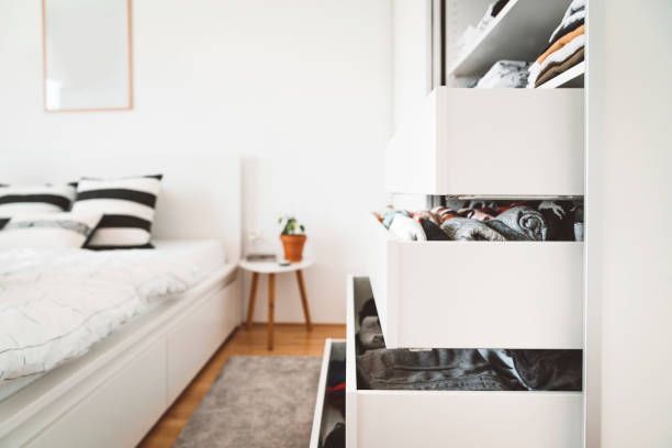 A bedroom with a bed and a closet with drawers filled with clothes.