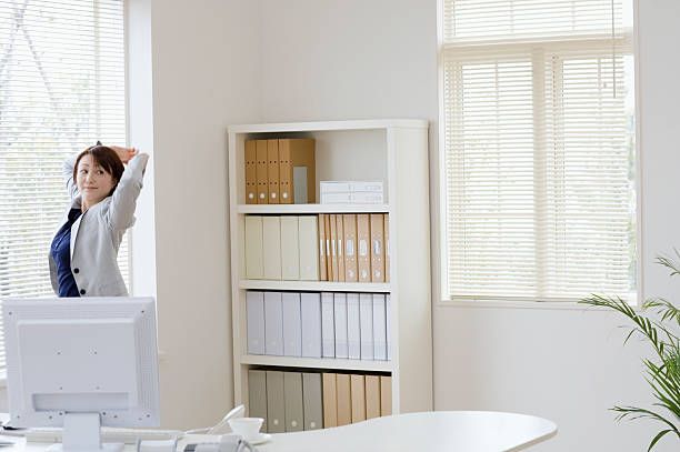 A woman is stretching her arms in front of a computer in an office.