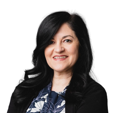 Woman with dark hair smiling, wearing a patterned blouse and black cardigan, against a gray background.