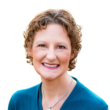 Woman with curly brown hair smiles, wearing teal top, necklace, and standing outside.