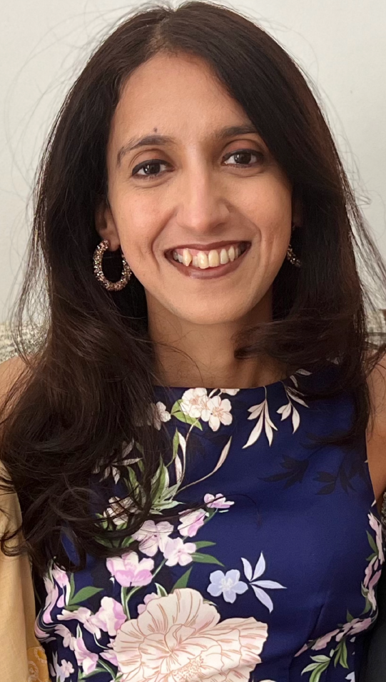 Woman with dark hair smiles, wearing a floral dress and hoop earrings.