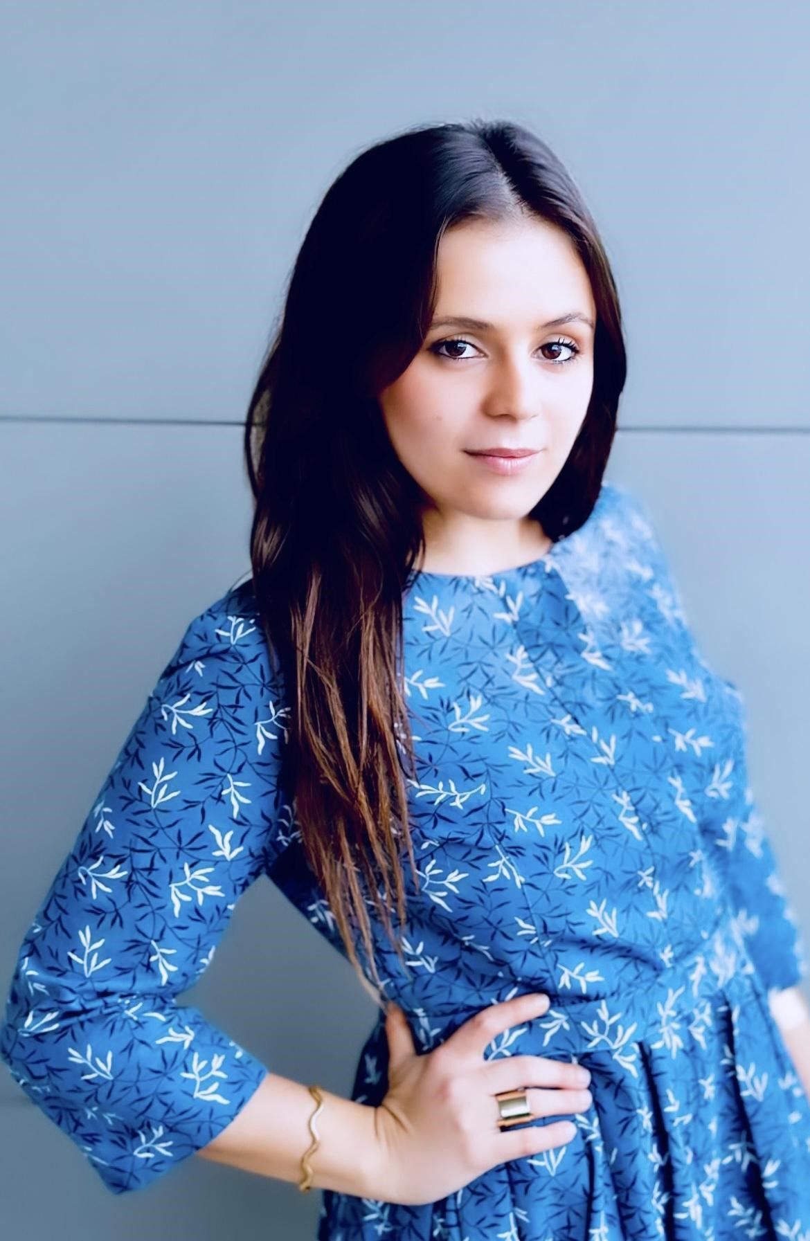 Woman in blue floral dress, hand on hip, looking at the viewer.