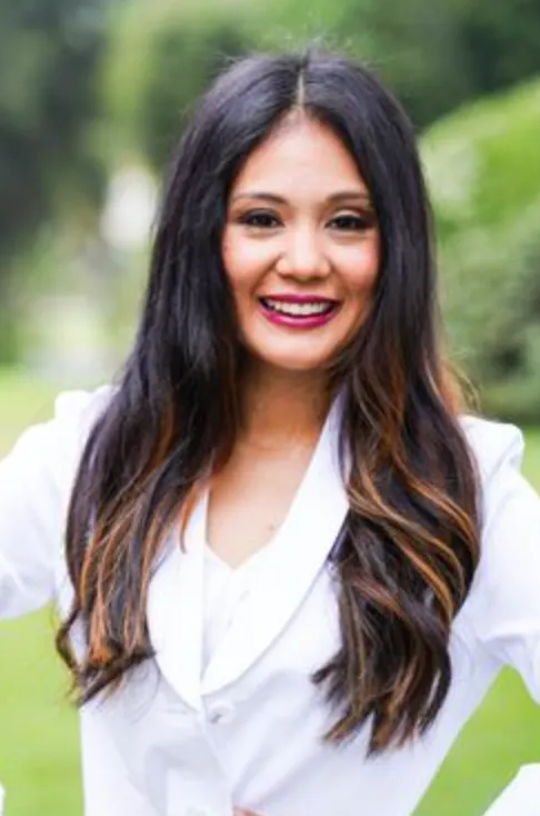 Woman smiling, wearing a white blazer, outdoors.