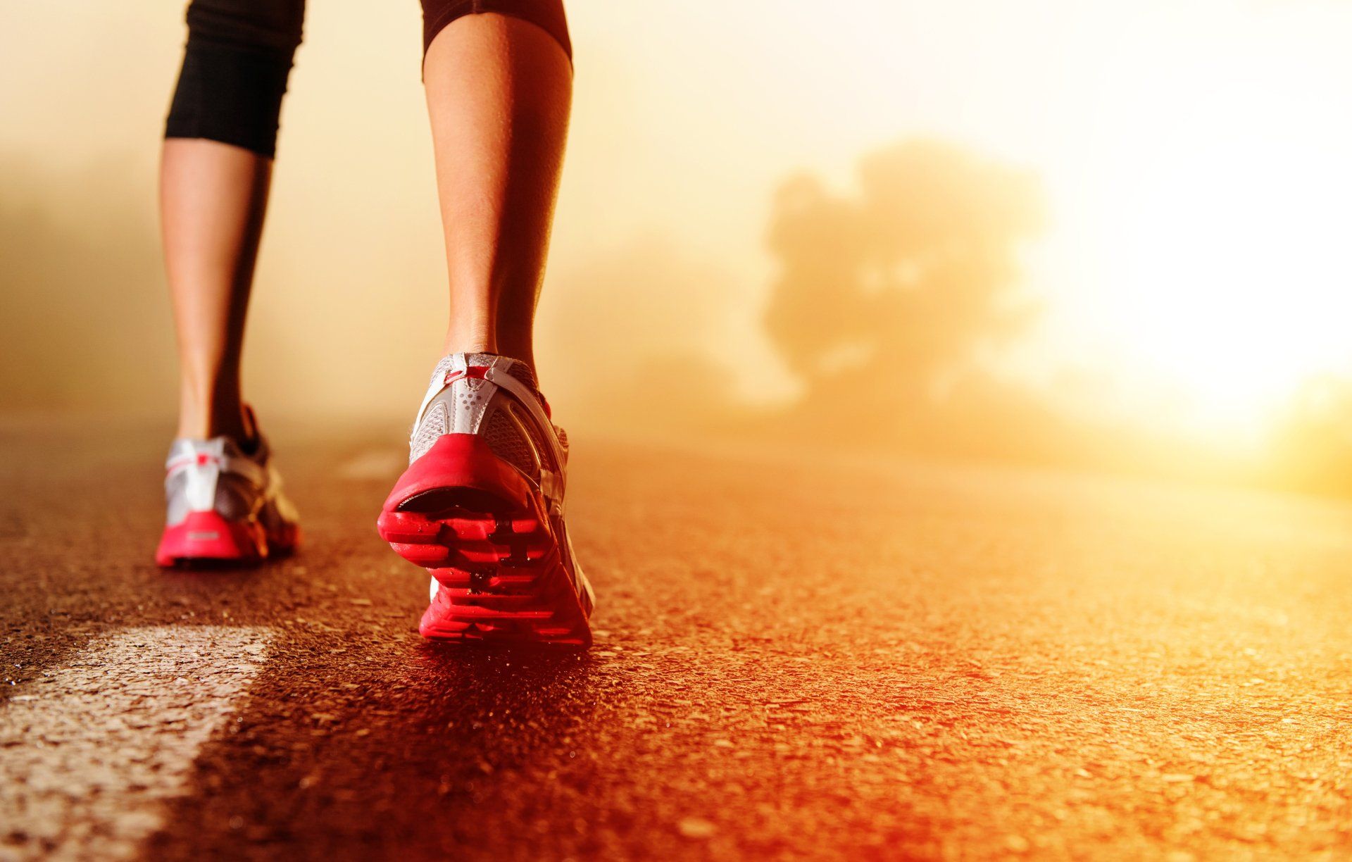 A closeup of a jogger's shoes from the back as they run on tarmac.