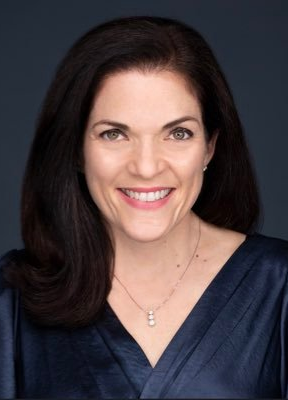 Woman with dark hair smiles, wearing a navy top and pendant necklace, against a dark blue background.