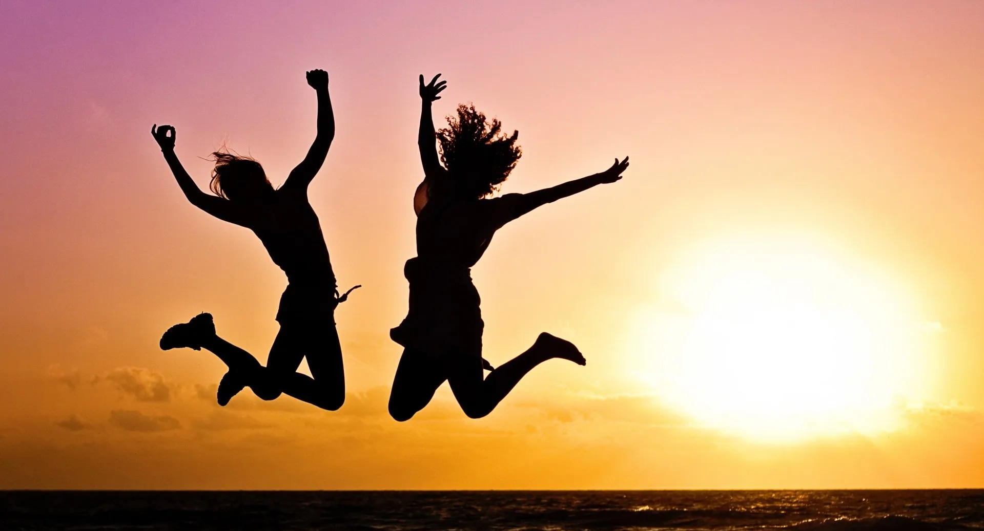 Silhoutte of two people jumping with joy with a sunset background.