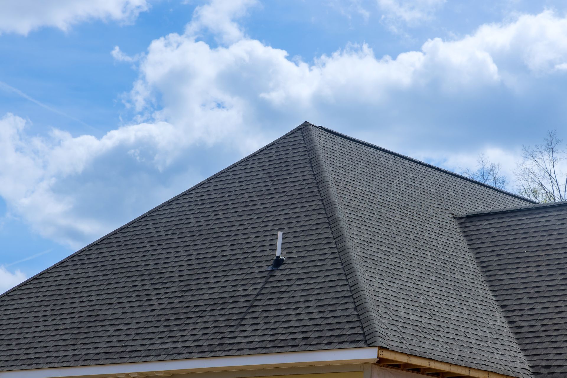 Gray shingled roof against a blue sky with white clouds.