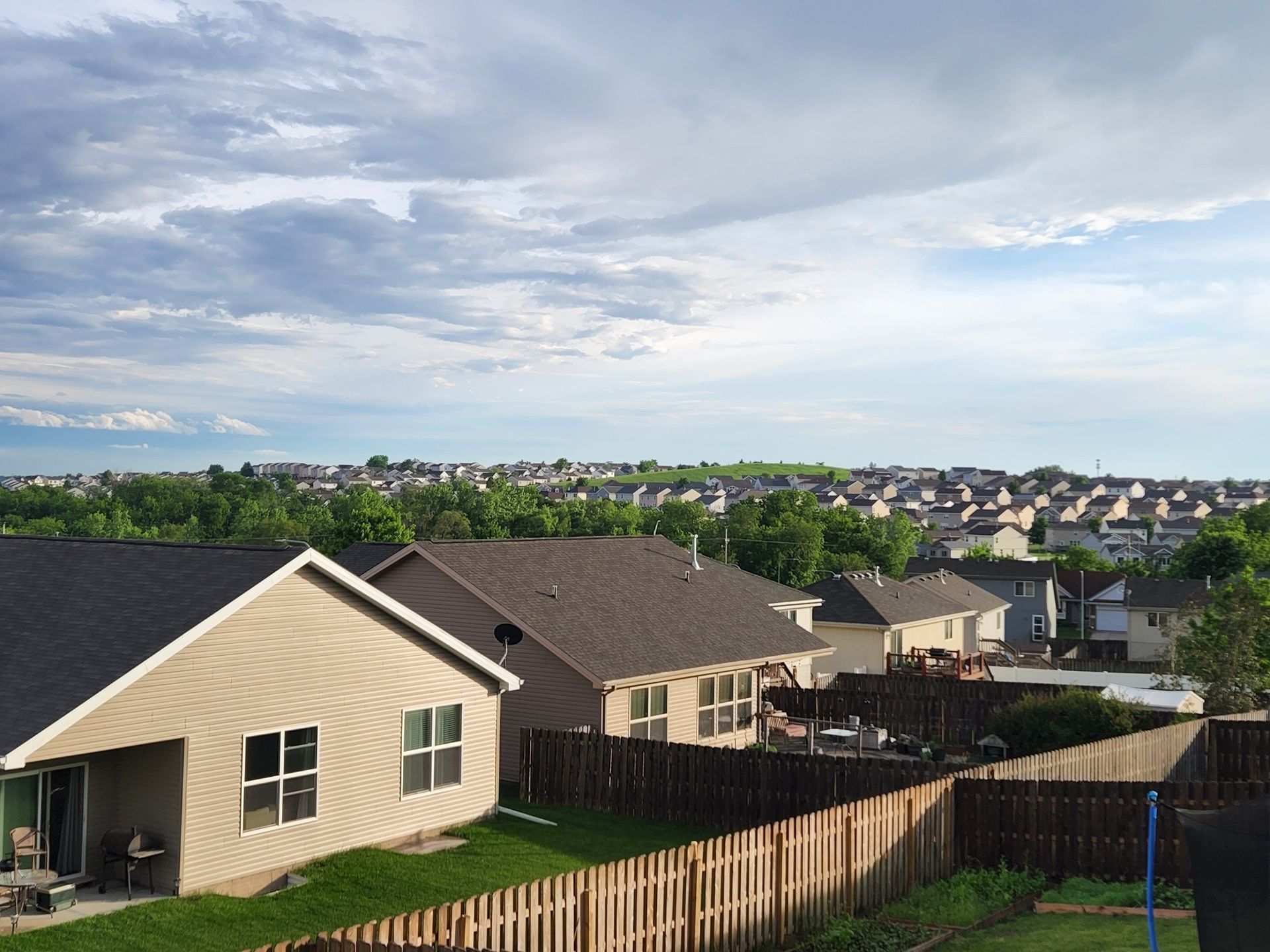 Residential neighborhood under a cloudy sky, with rows of houses and wooden fences. Green lawns.