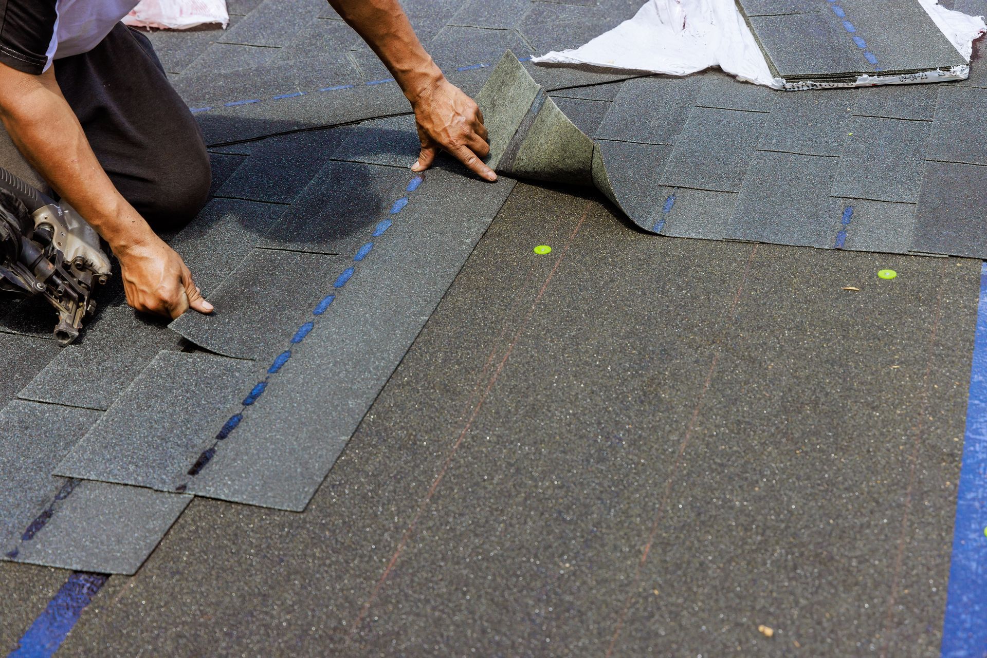 Person installing asphalt shingles on a roof, revealing the underlayment.