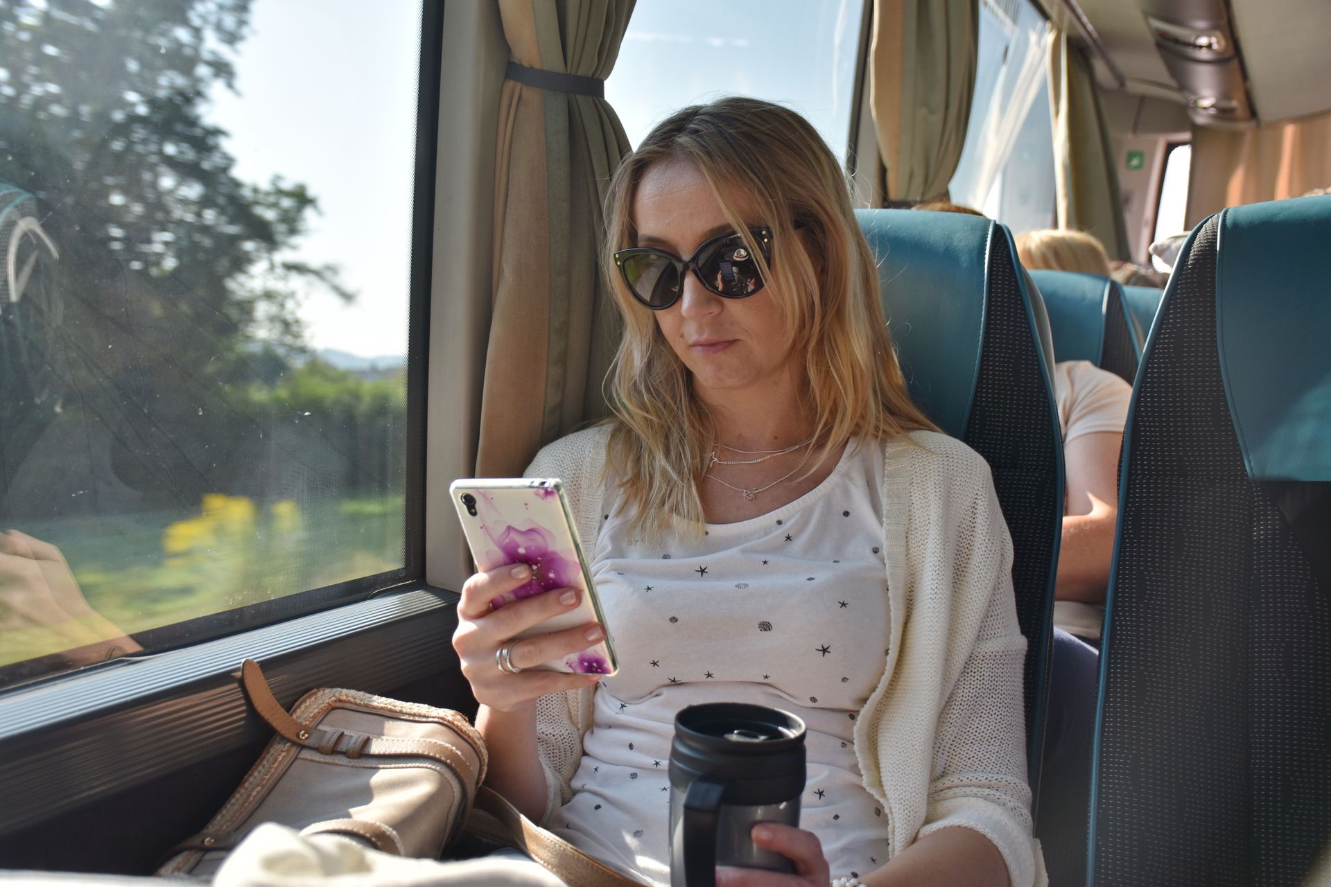 Mulher em um ônibus olhando para o celular, usando óculos escuros.