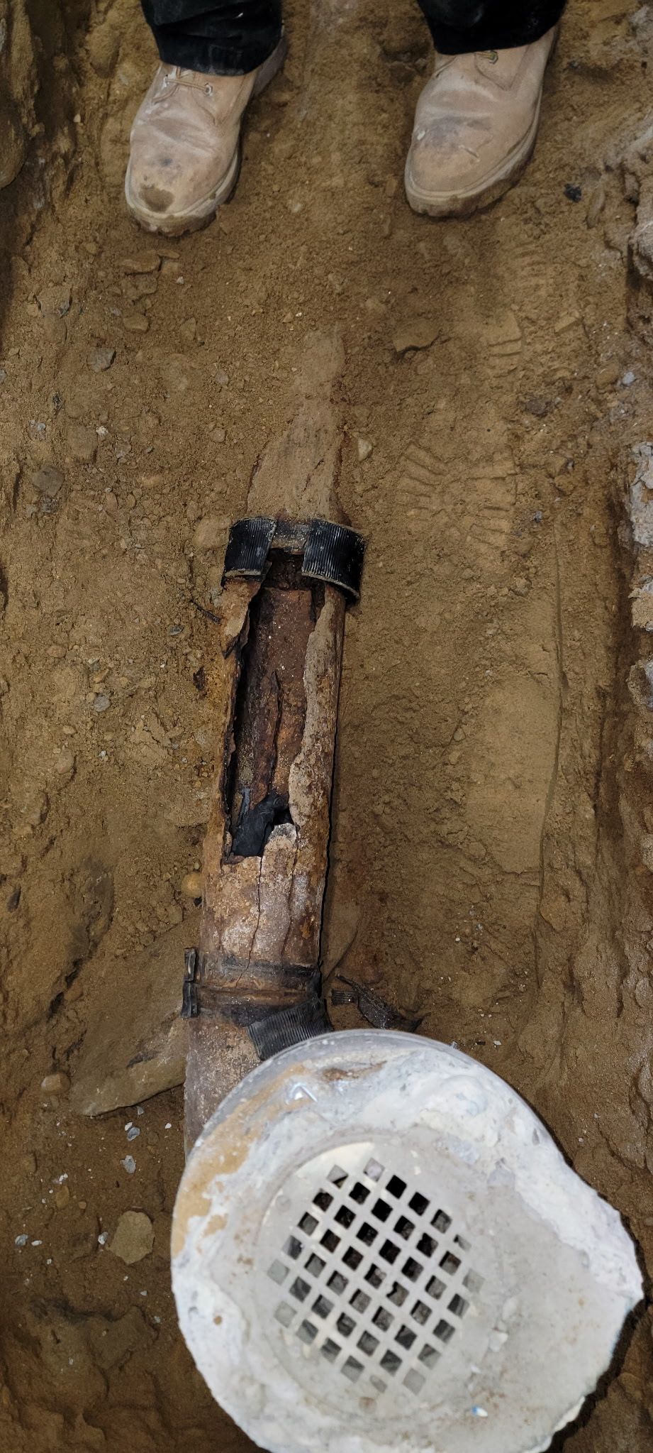 A person is standing next to a drain pipe in the dirt.