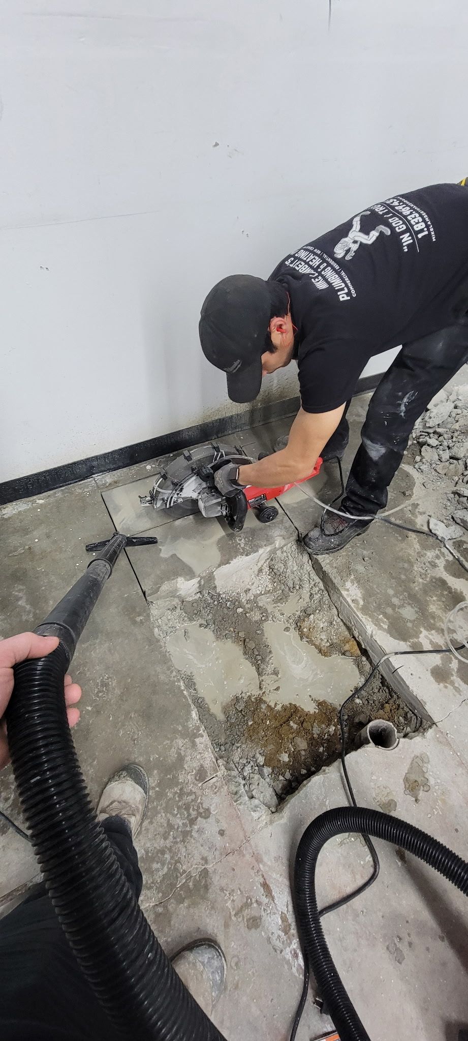 A man is working on a concrete floor with a vacuum cleaner.