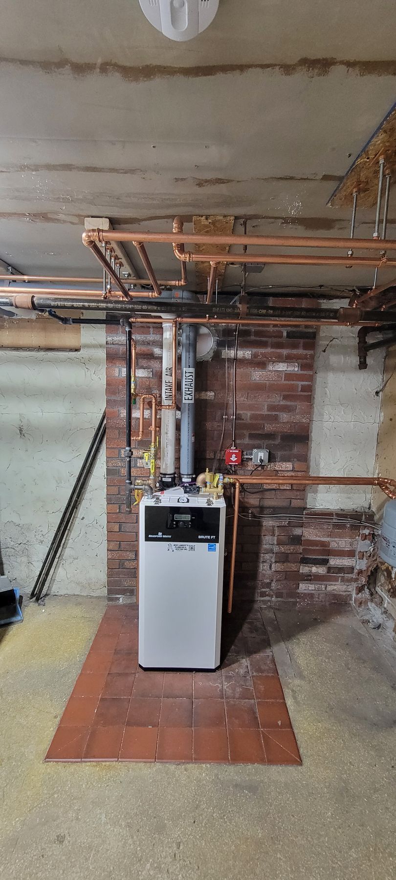 A boiler is sitting in a basement next to a brick wall.
