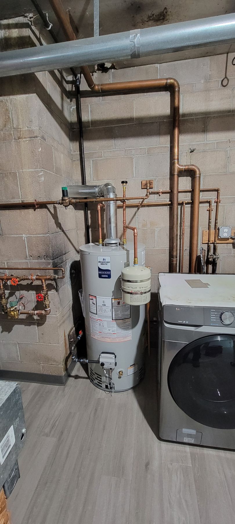A water heater is sitting next to a washer and dryer in a laundry room.