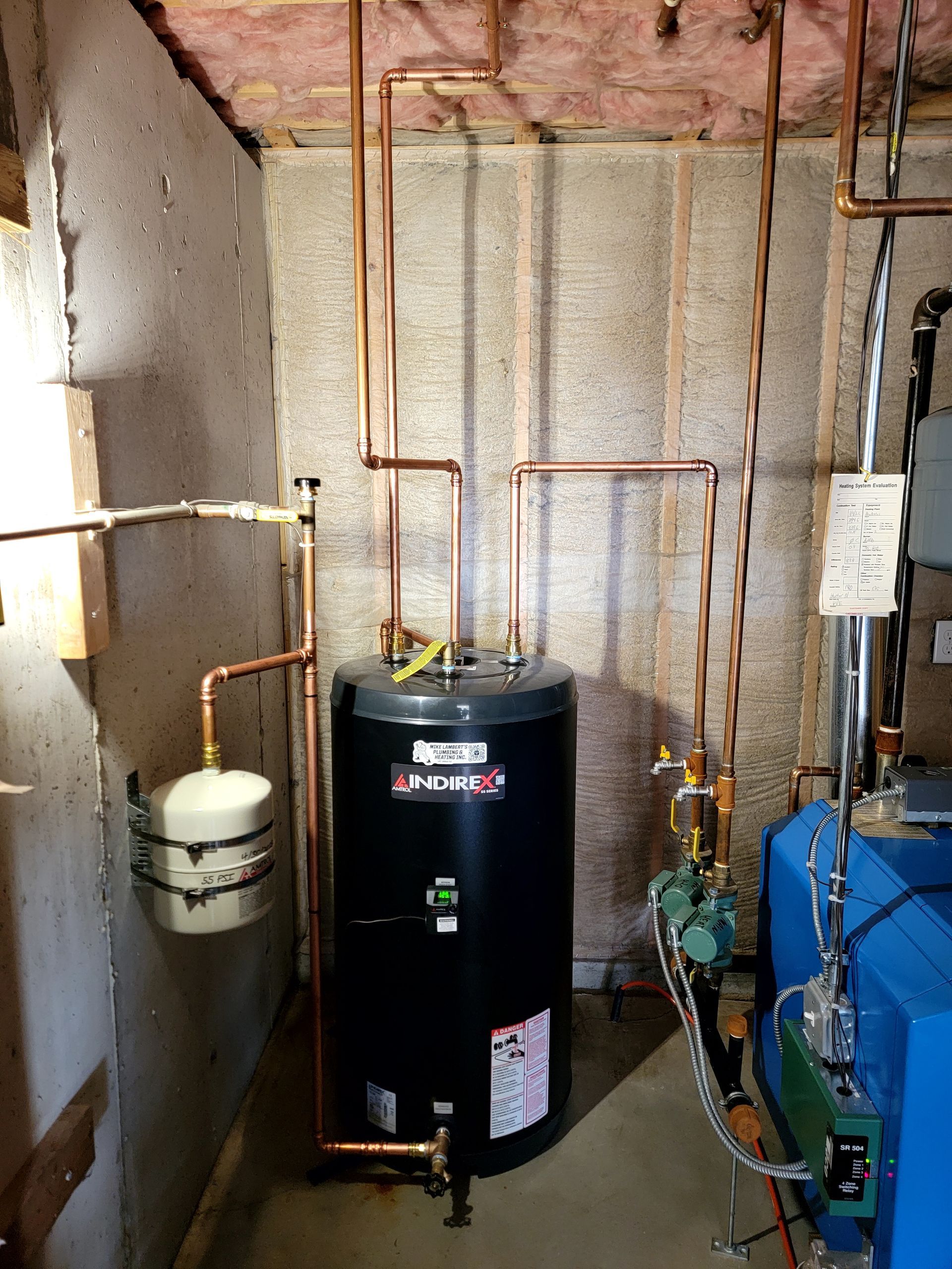 A black water heater is in a basement next to a blue boiler