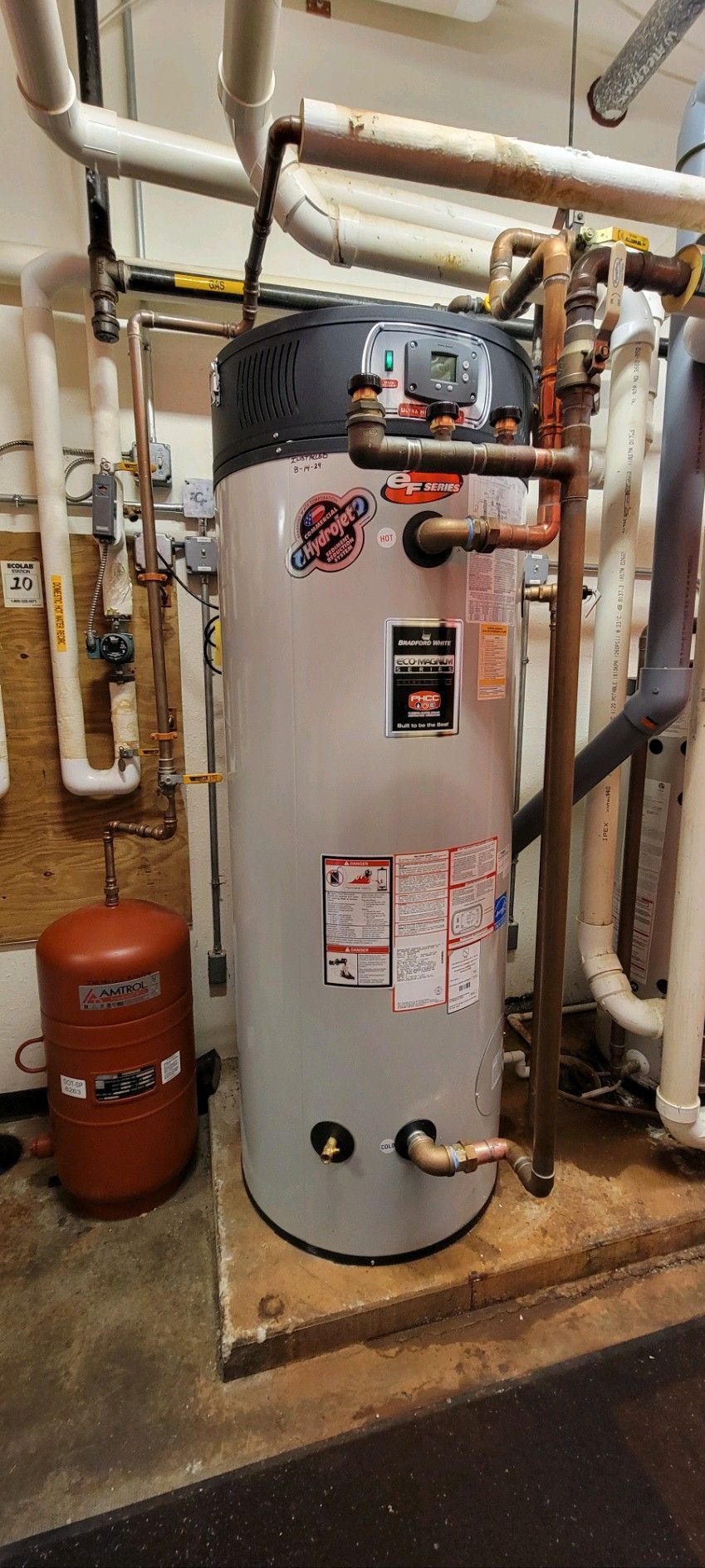 A large water heater is sitting in a room with pipes.