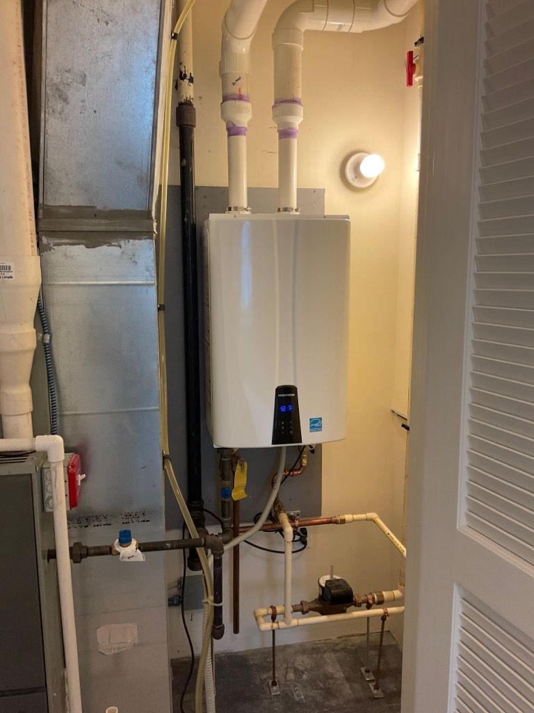A white water heater is sitting in a room next to a pipe.