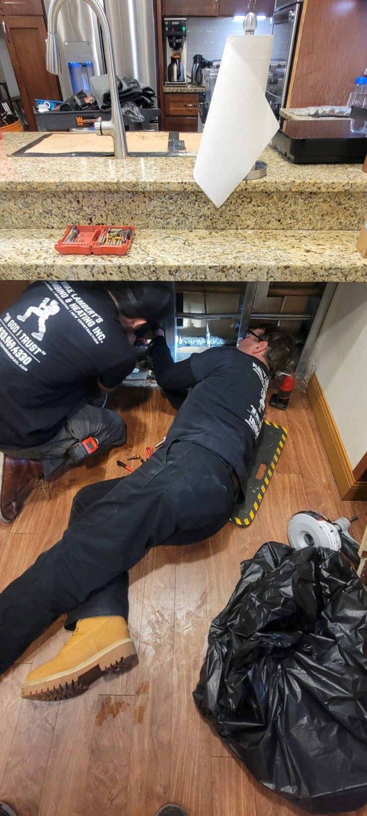 Two men are working under a sink in a kitchen.