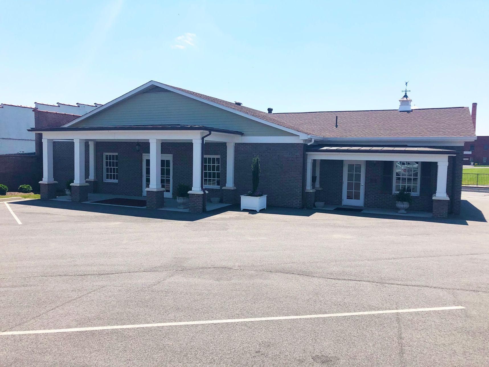 A large brick building with a porch and a parking lot in front of it.