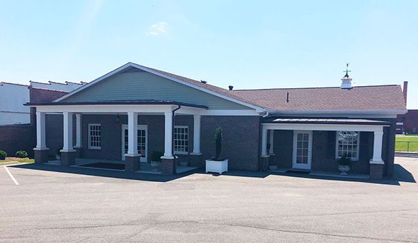 A large brick building with a porch is sitting in a parking lot.