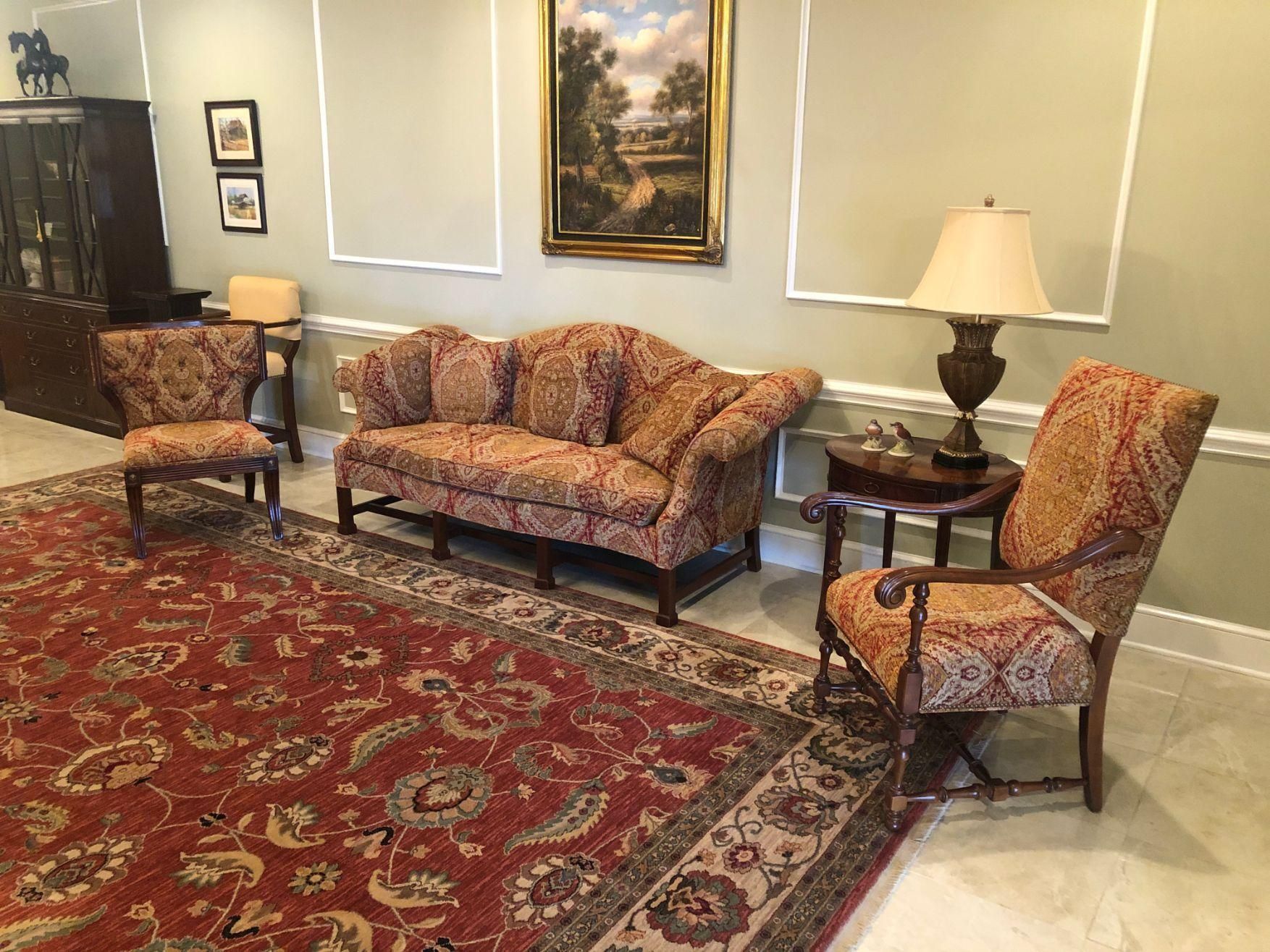 A living room with a couch , chairs , lamps and a rug.