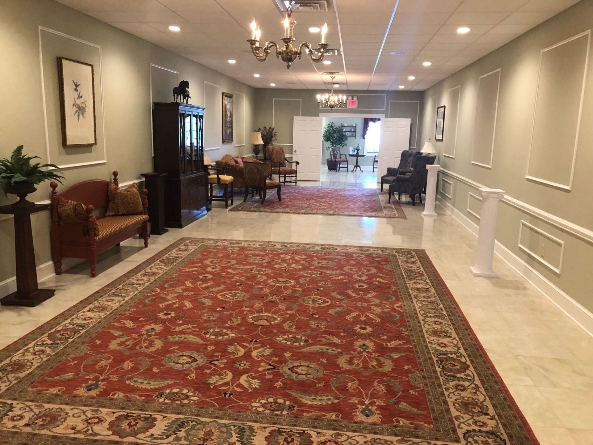 A long hallway with a red rug , chairs , and a chandelier.
