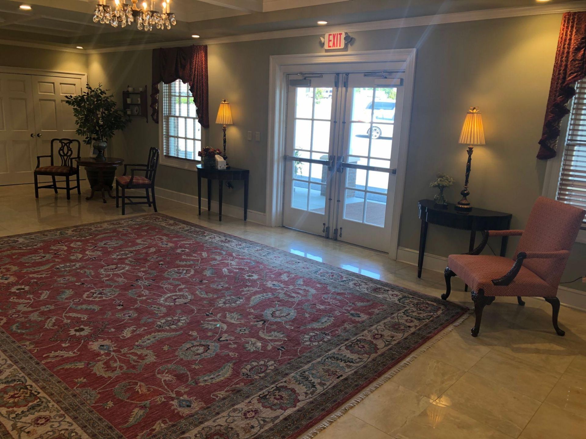 A living room with a red rug , chairs , tables and lamps.