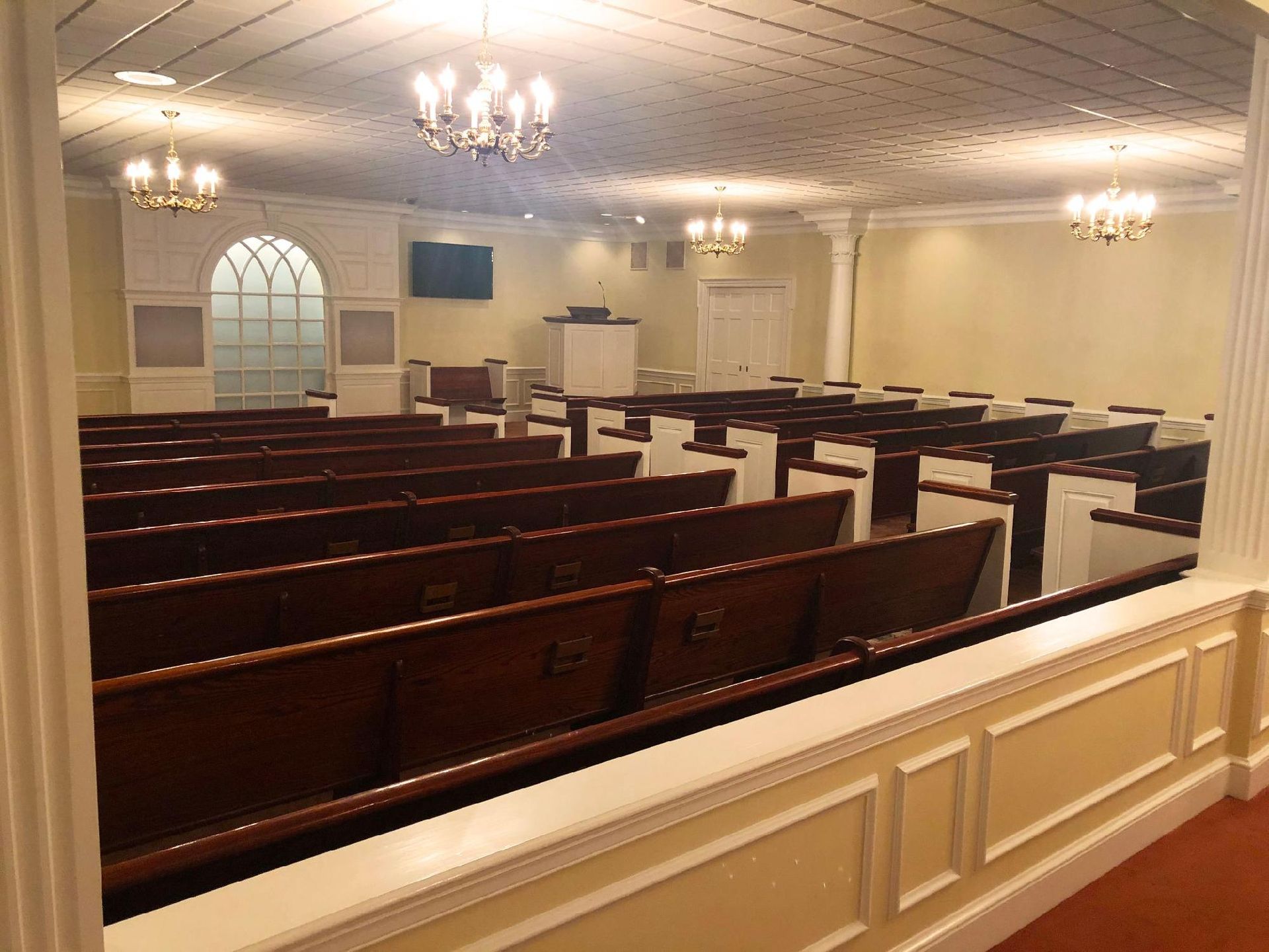 A church with rows of wooden benches and a chandelier hanging from the ceiling.