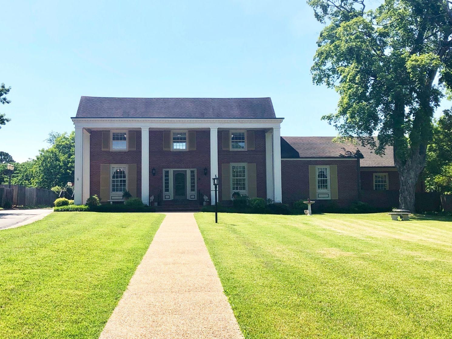 A large brick house with a lush green lawn and a walkway leading to it.