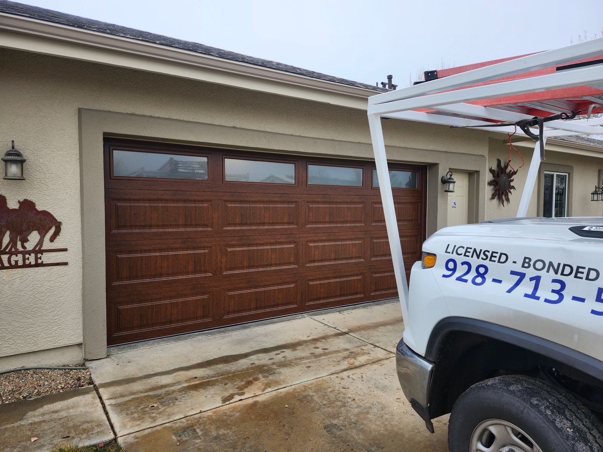 Brown garage door with windows, tan stucco house, and a white service truck.