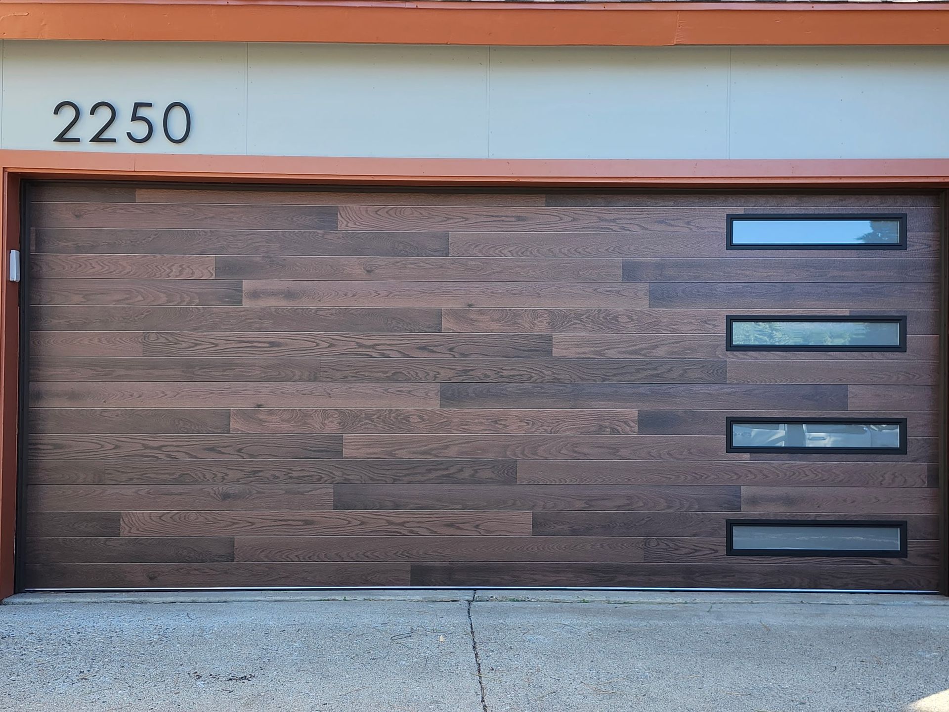 Modern garage door with horizontal woodgrain panels, four rectangular windows, and address 