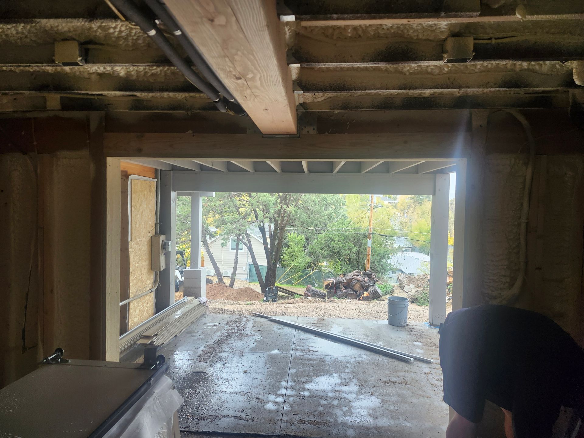 Interior view of a garage opening onto a yard. Construction is in progress.