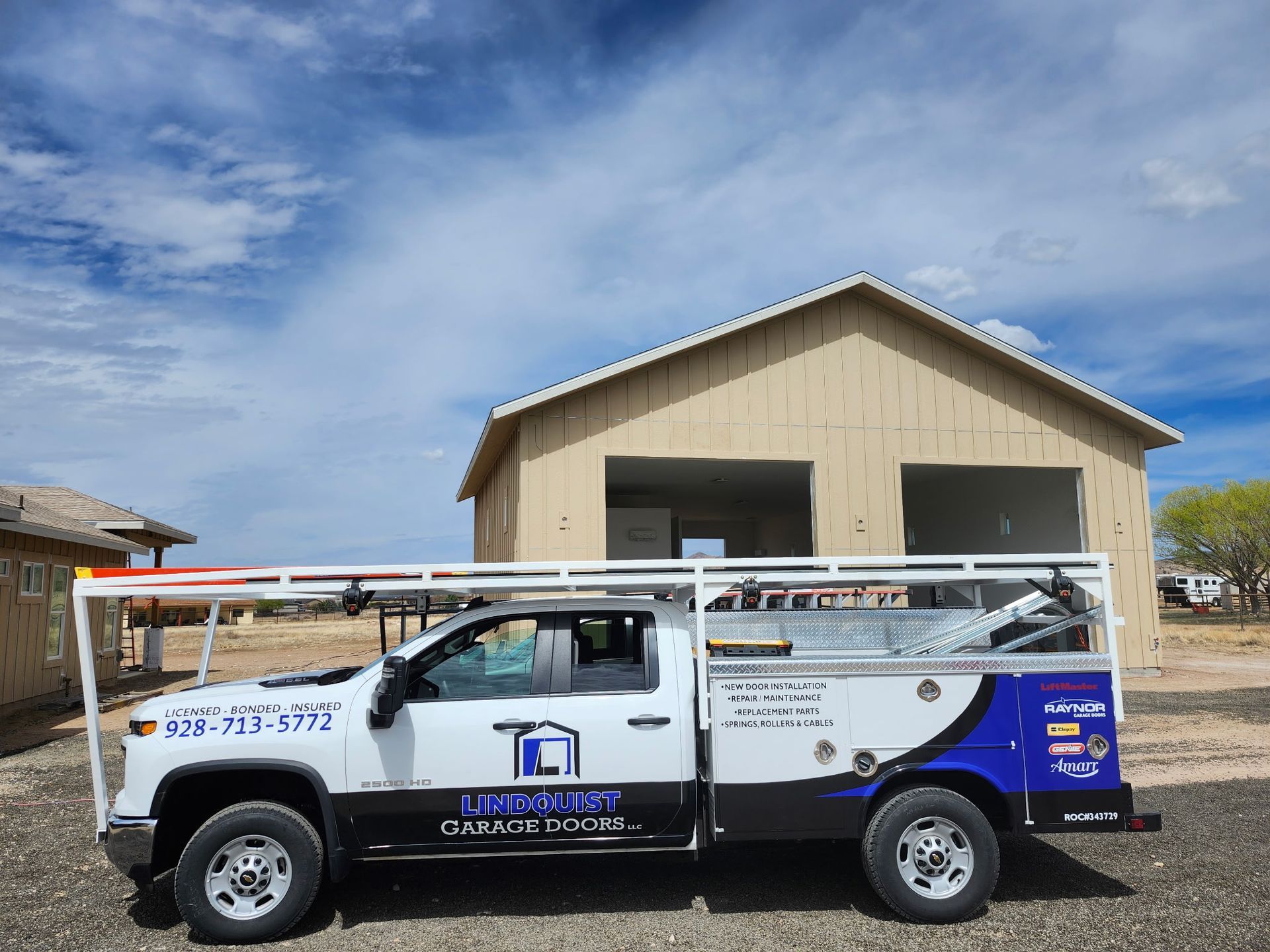 Service truck parked in front of a construction site. Truck is white and blue with company logo; building is light tan.